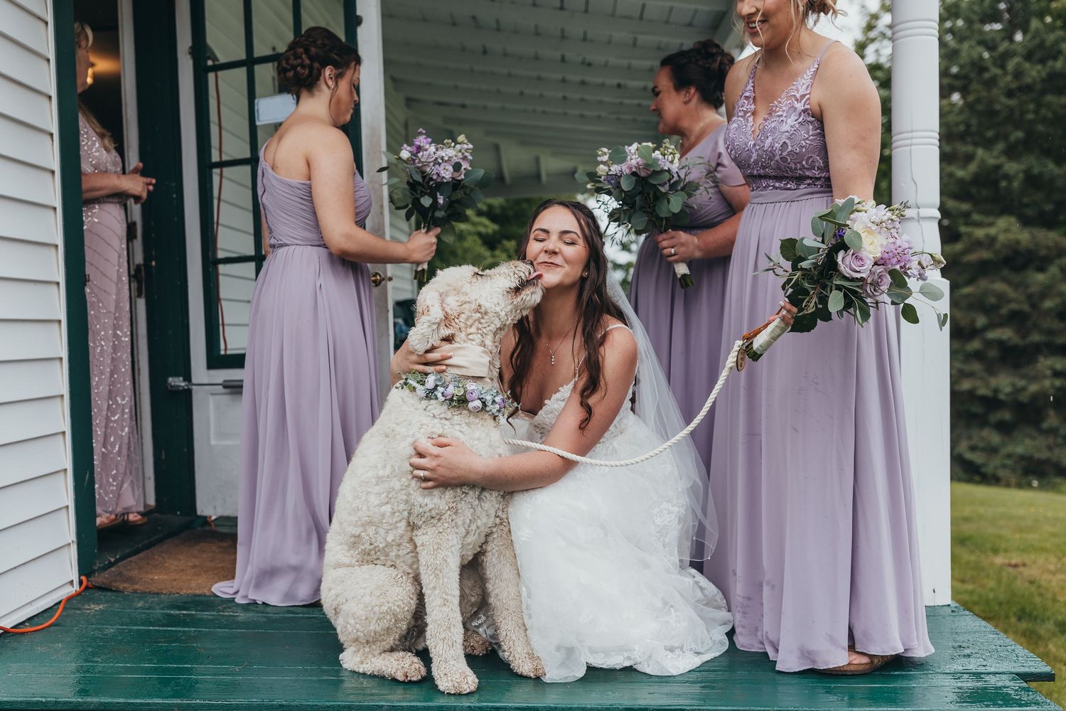 Wedding party in lavender dresses posing on a white porch.