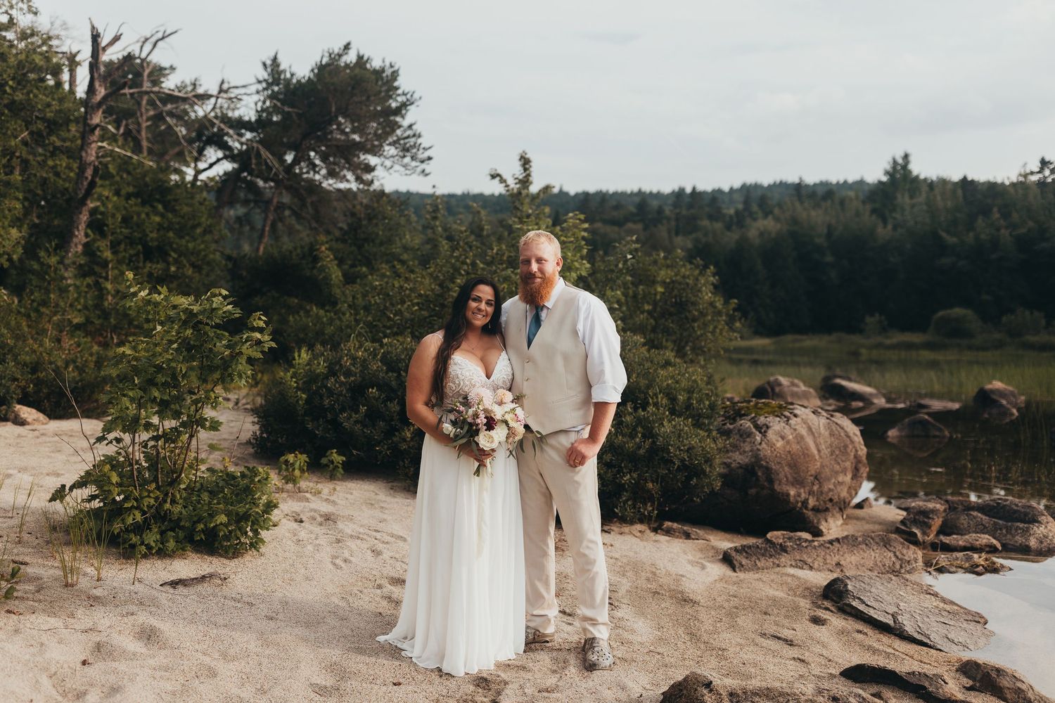 Scenic coastal wedding photos taken on a rocky beach surrounded by evergreen trees.