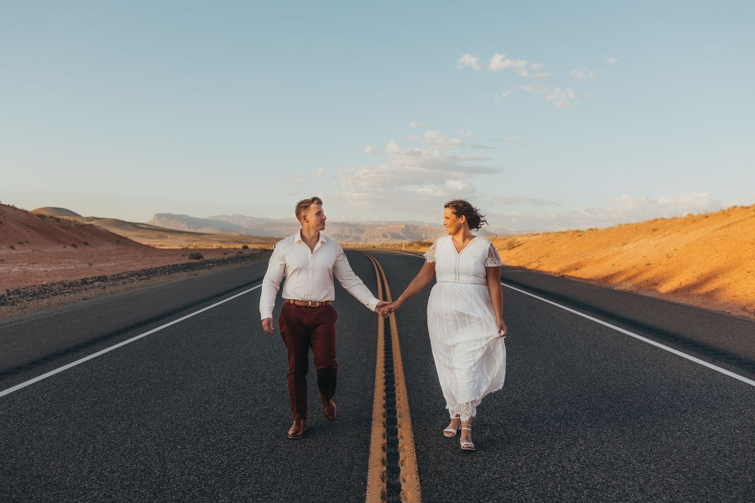 Couple walking and posing on an empty desert road during golden hour.