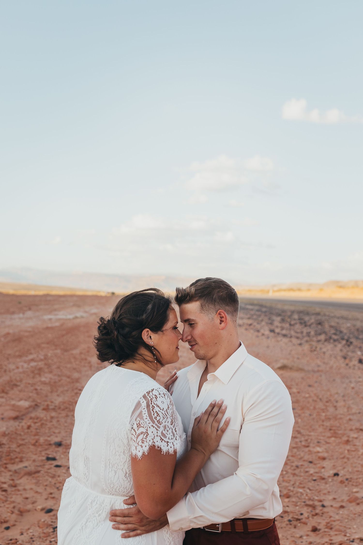 Romantic desert photoshoot with white lace dress against warm orange landscape.