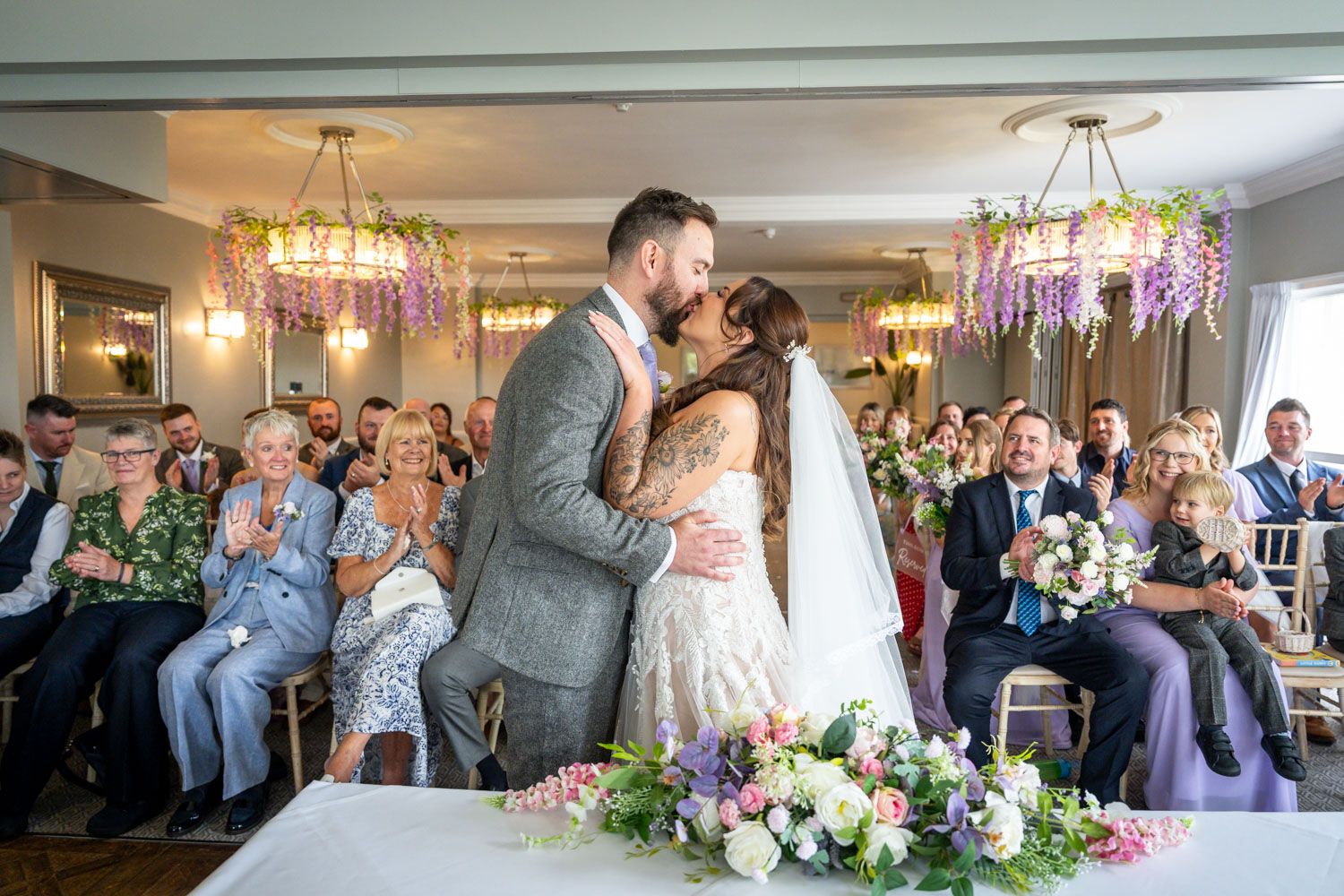 Newlyweds share their first kiss at the altar surrounded by applauding wedding guests.