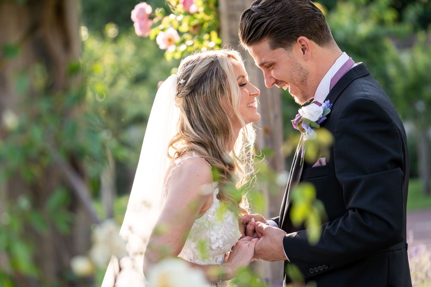 Intimate garden wedding moment captured among blooming pink flowers and greenery.