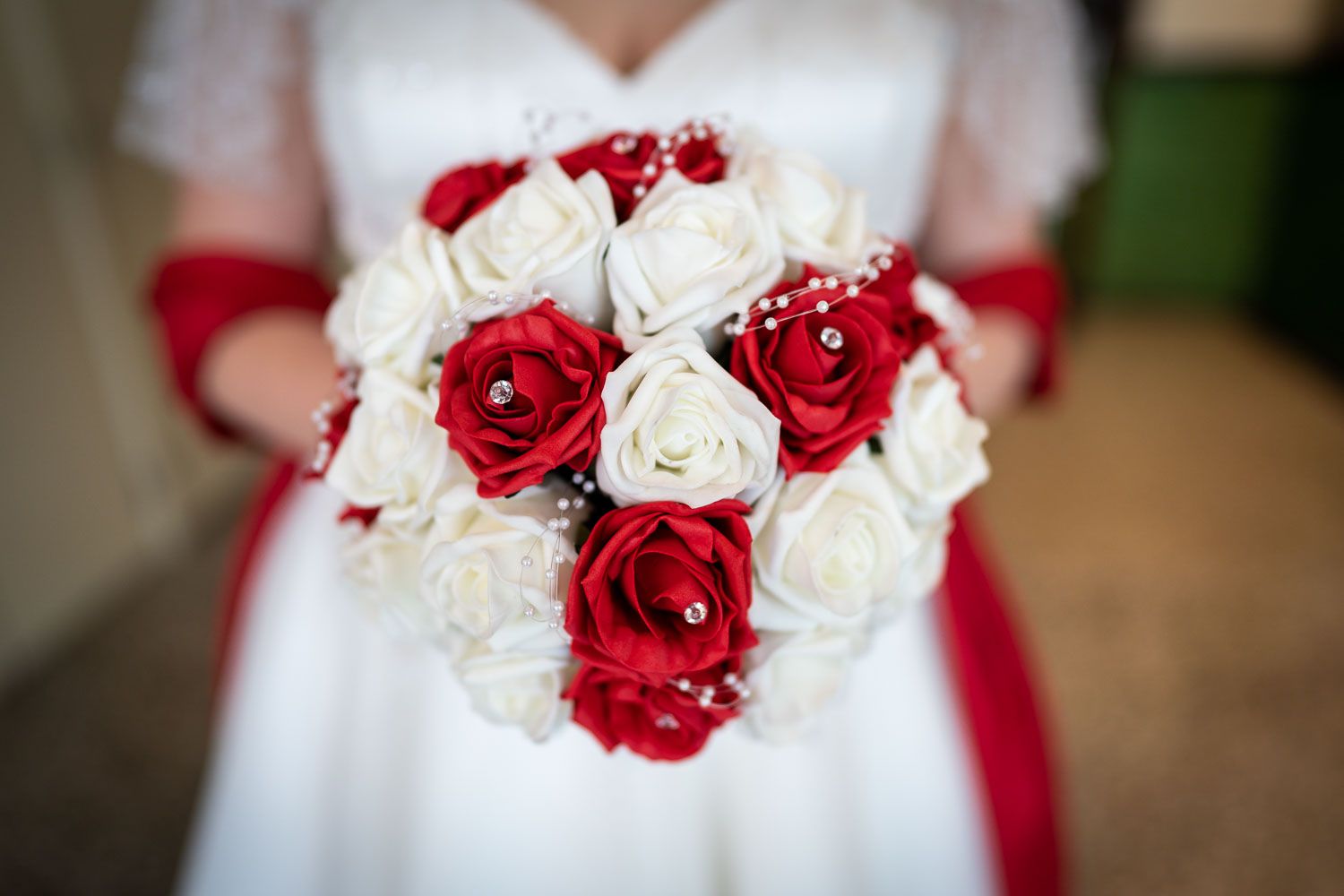 Beautiful bridal bouquet featuring red and white roses tied with a red ribbon against a white gown background.
