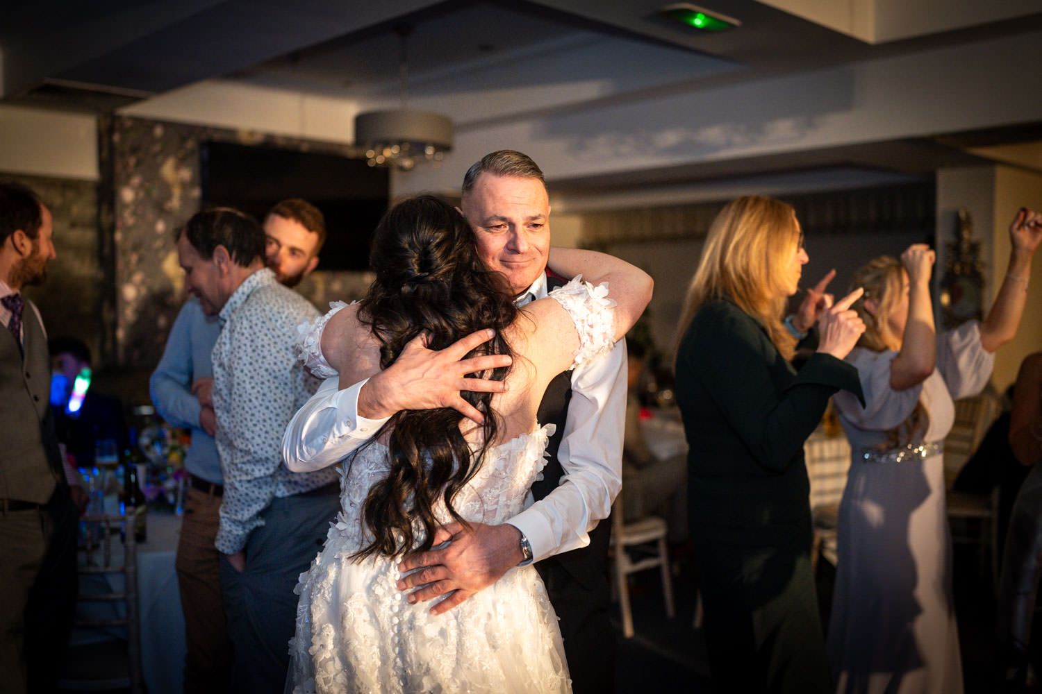 A couple shares an intimate dance at their wedding reception while other guests dance in the background.