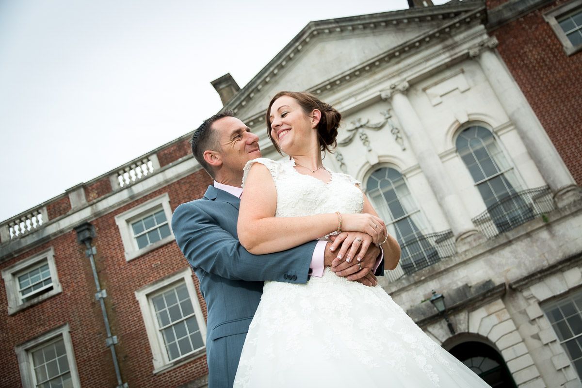 Happy newlyweds sharing a joyful embrace outside a stately brick and stone building with classic architecture.