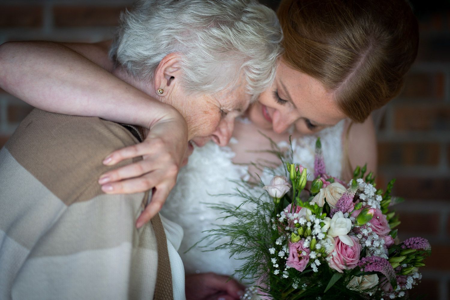 A tender moment shared between two people at a wedding, with a pink and purple floral bouquet visible in the scene.
