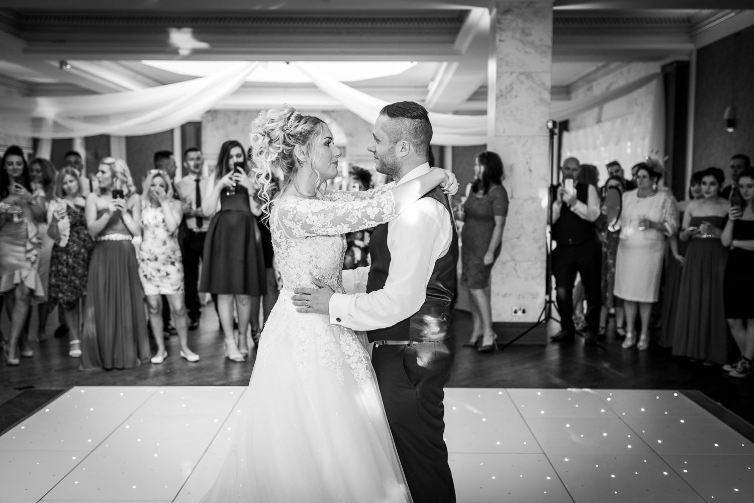 A couple shares their first dance at their wedding reception on an illuminated dance floor while guests watch from the sidelines.