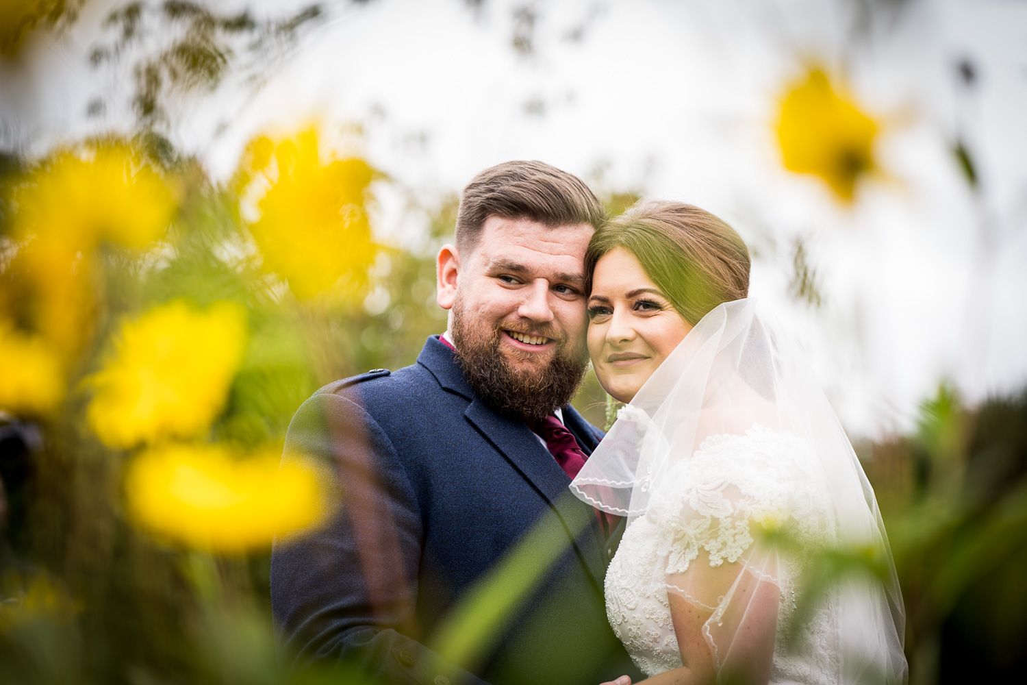 A couple poses among yellow flowers on their wedding day in soft focus.