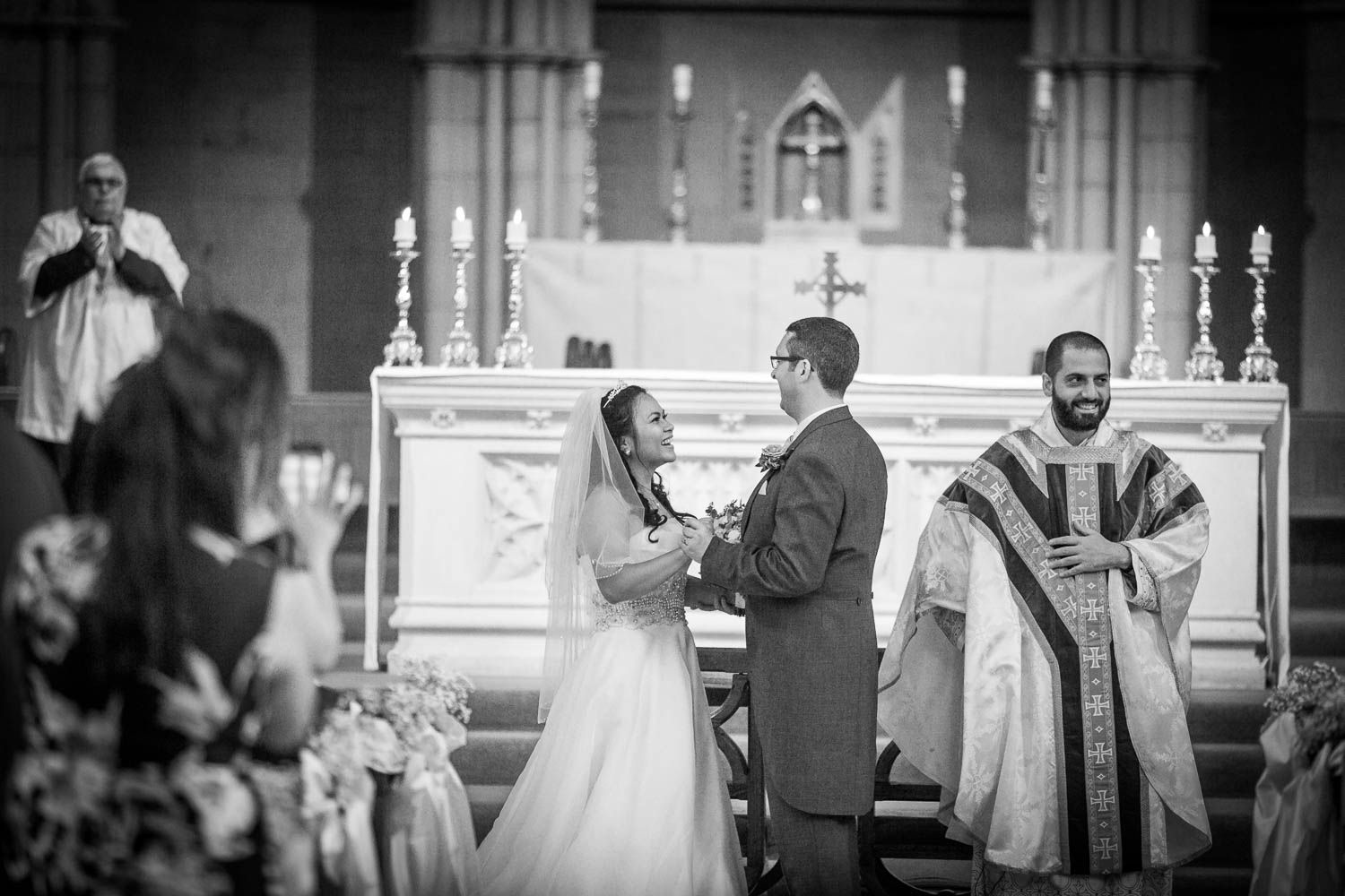 A black and white photograph capturing a wedding ceremony at a traditional church altar with ornate decor.