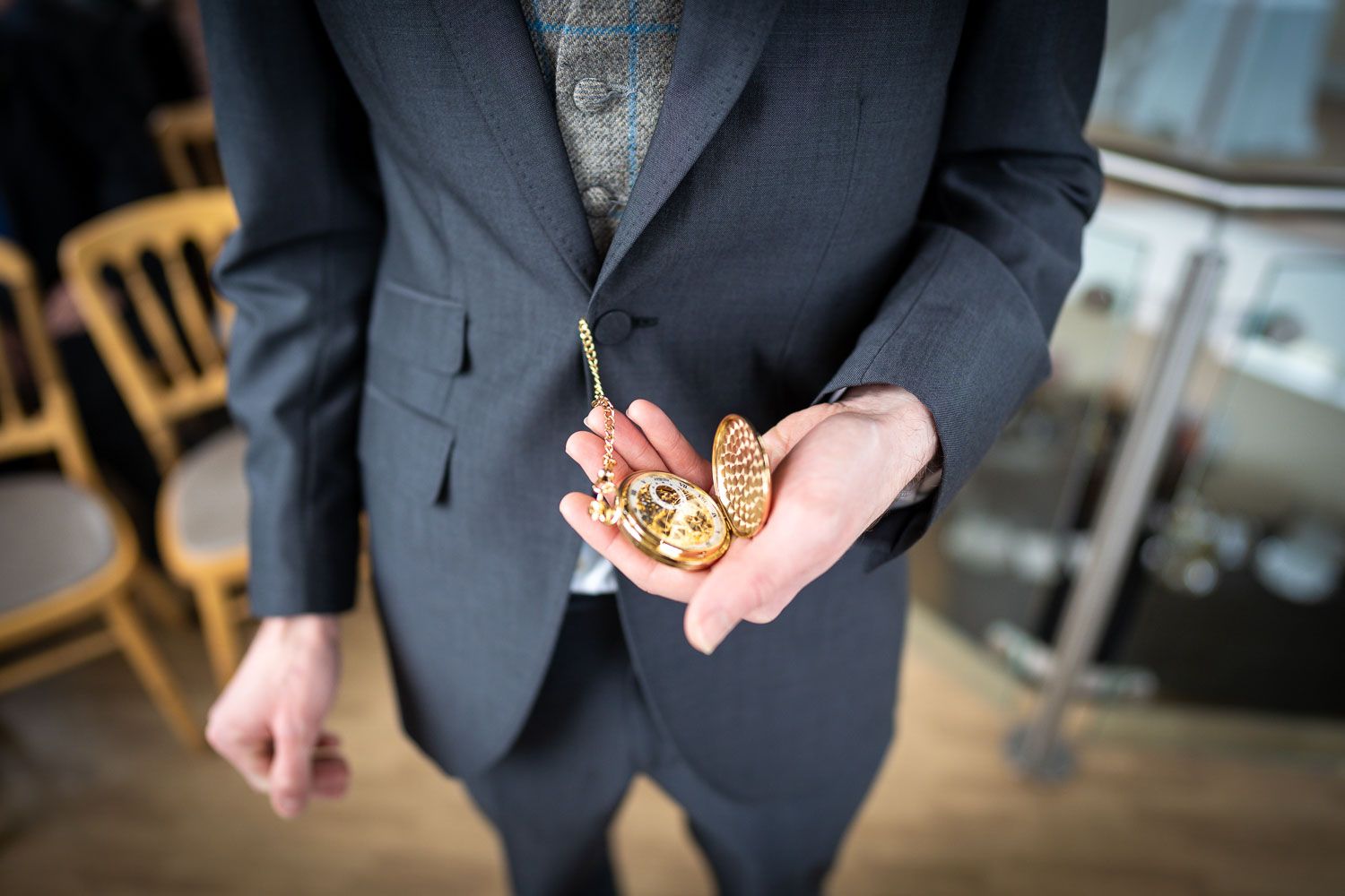 Hands in formal suit attire holding gold wedding rings against an indoor venue background.