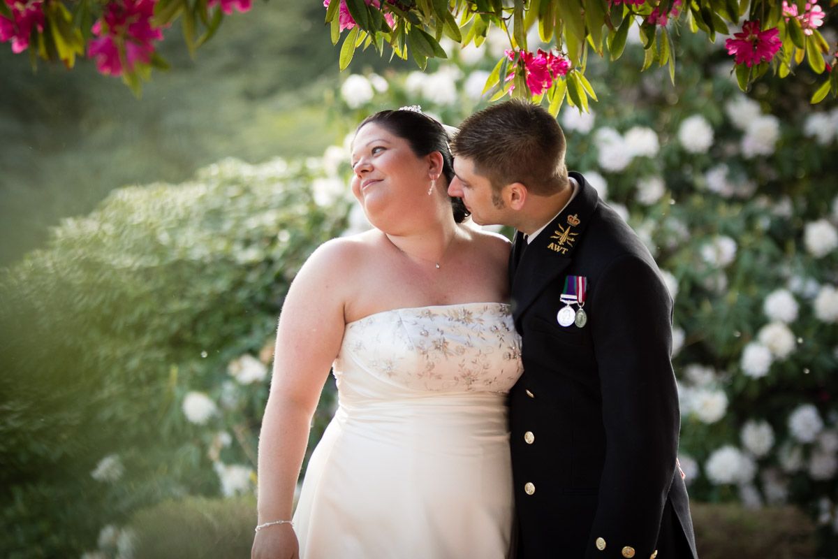 Newlyweds share an intimate moment in a garden surrounded by blooming pink and white flowers.