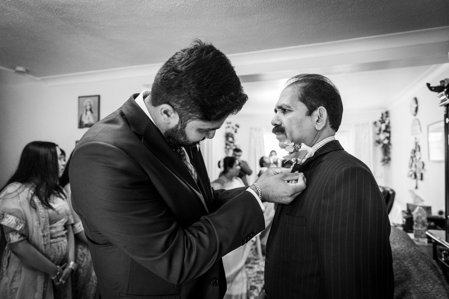 A black and white photograph showing aid being given in adjusting formal attire during a special occasion indoors.