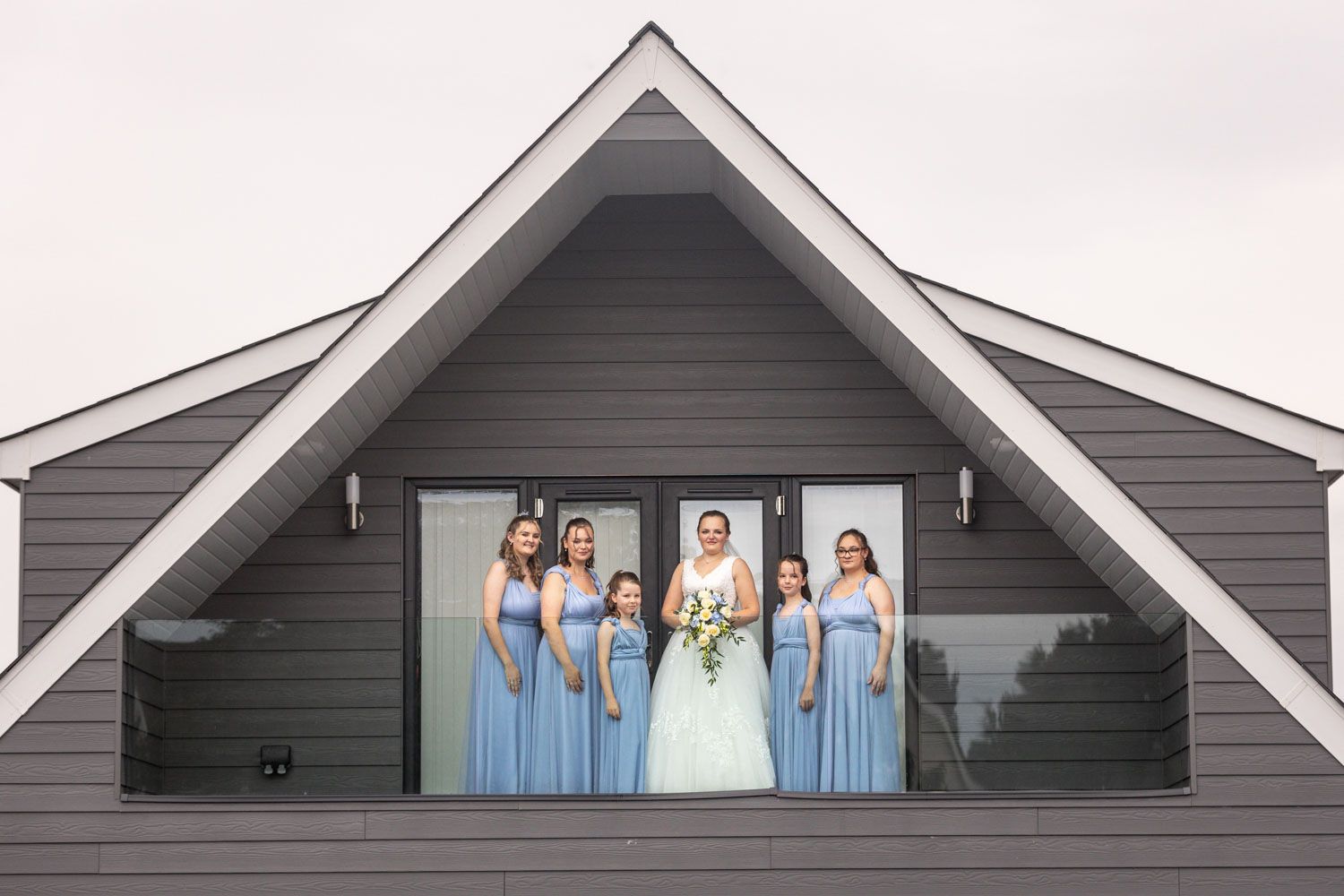 Wedding party poses in light blue bridesmaid dresses and white gown framed by gray architectural triangle.