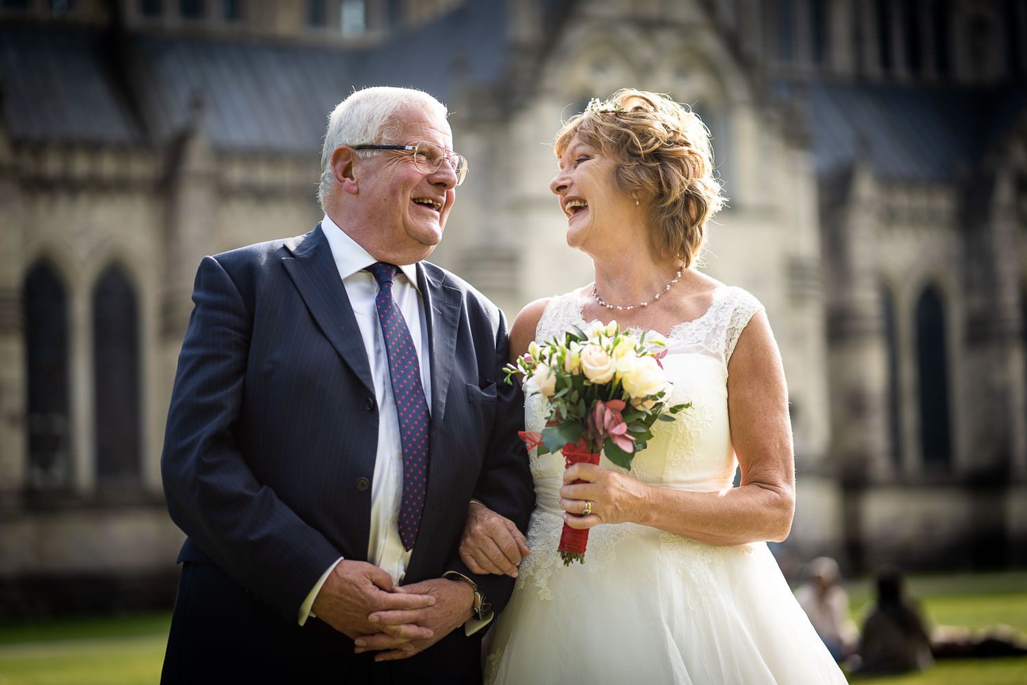 A happy moment at a wedding with a bride in white dress holding a bouquet outside a historic stone church building.
