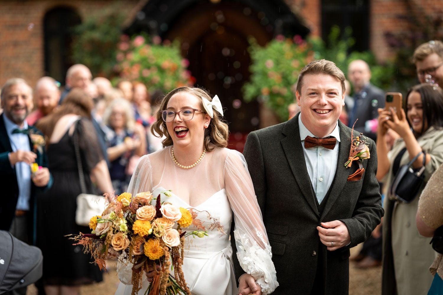 A joyful newlywed couple walking down the aisle together while holding a vibrant orange and yellow bouquet.
