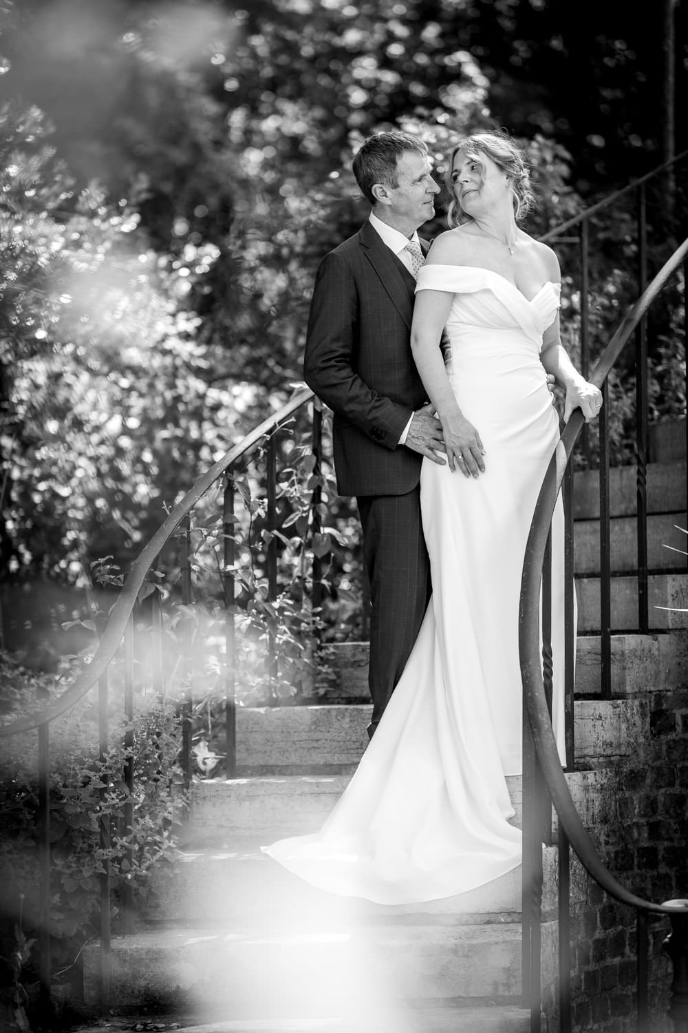 Black and white portrait of bride and groom embracing on garden steps in romantic pose.