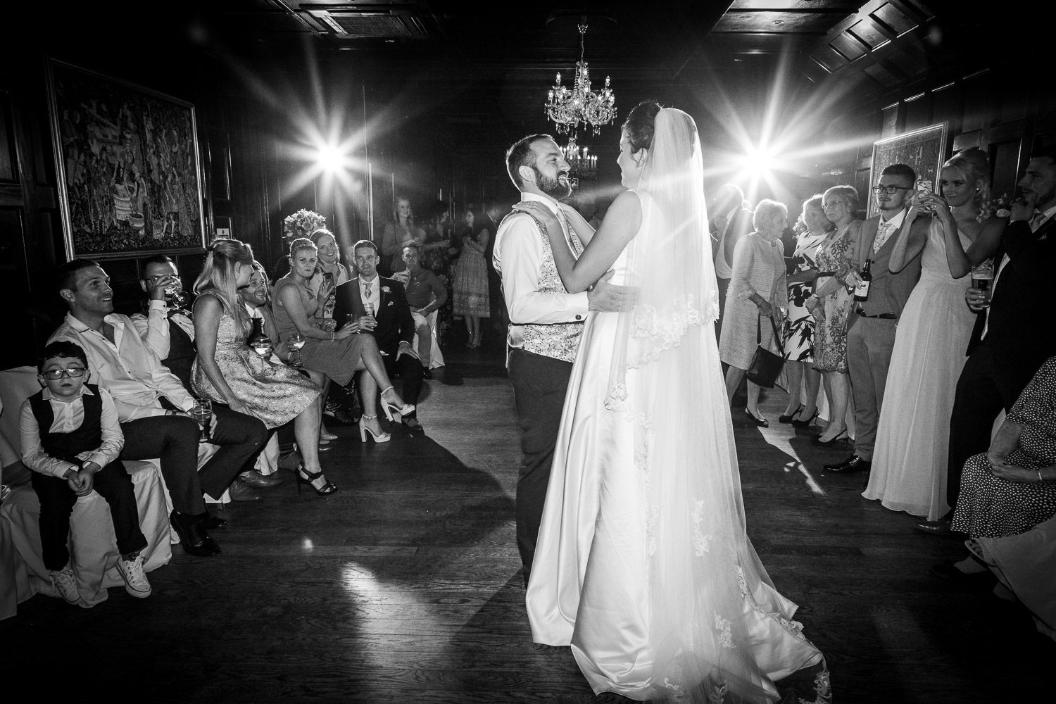A romantic first dance at a wedding reception captured in black and white with guests watching from the sides.