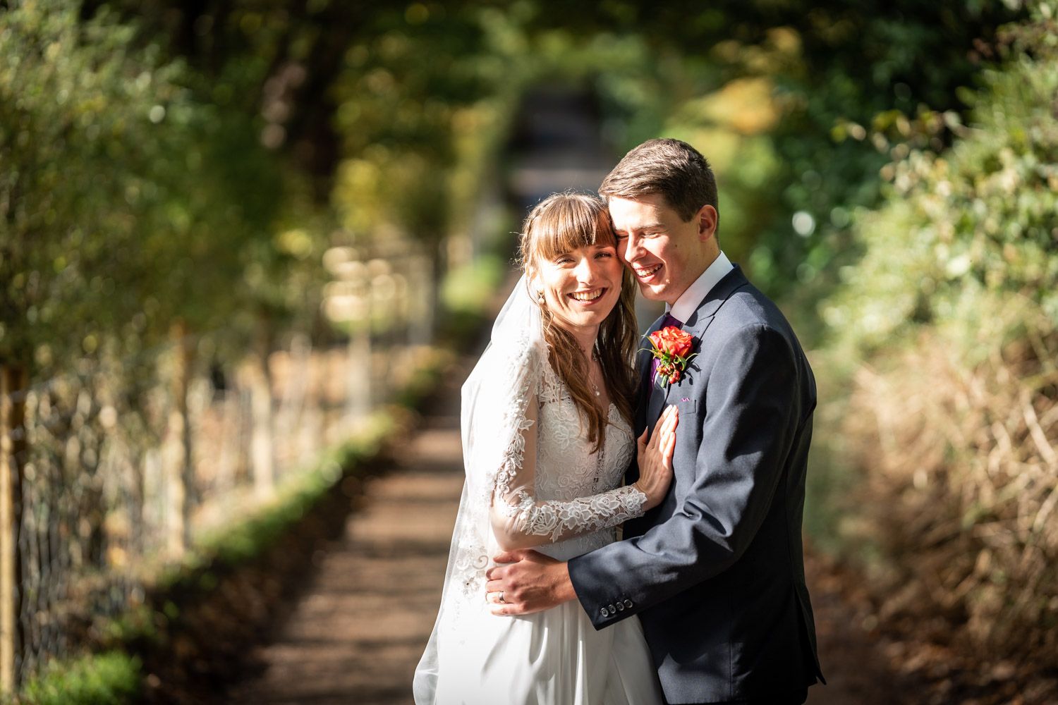 A happy couple embraces on a tree-lined path during their autumn wedding celebration.
