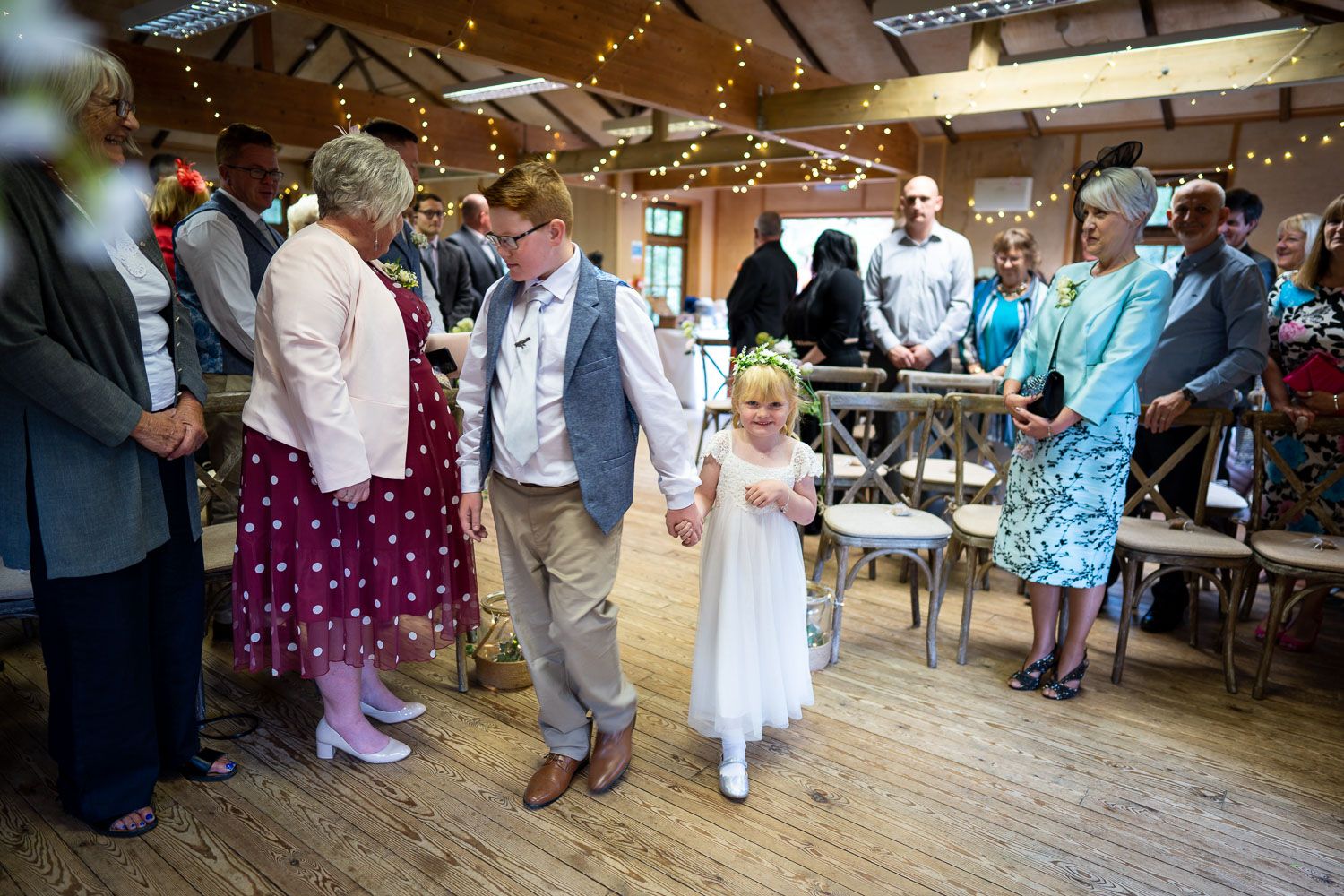 A festive wedding reception with guests dancing under twinkle lights in a rustic wooden venue.