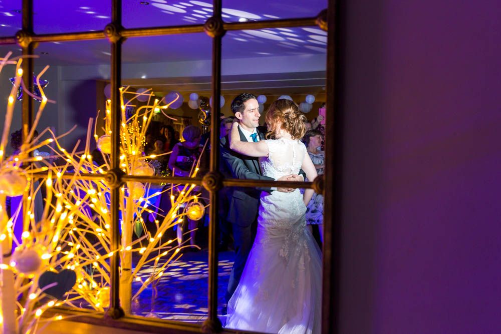 A couple shares their first dance at a wedding reception with glowing yellow decor and blue uplighting in the background.