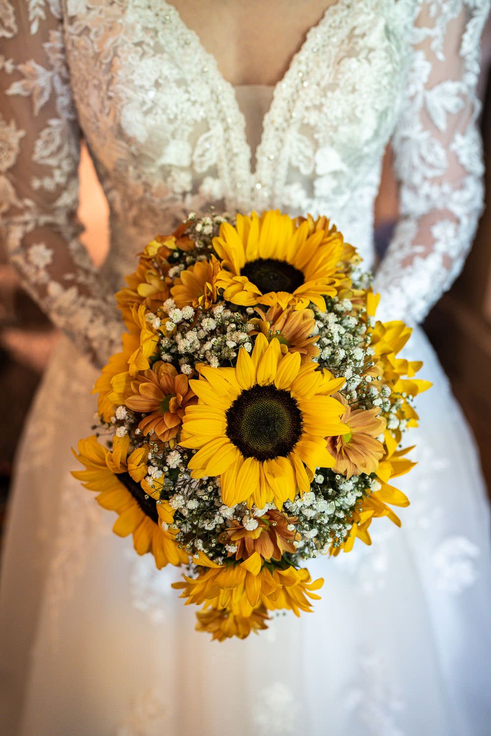 Wedding bouquet of bright yellow sunflowers and white baby's breath against a white lace wedding dress.