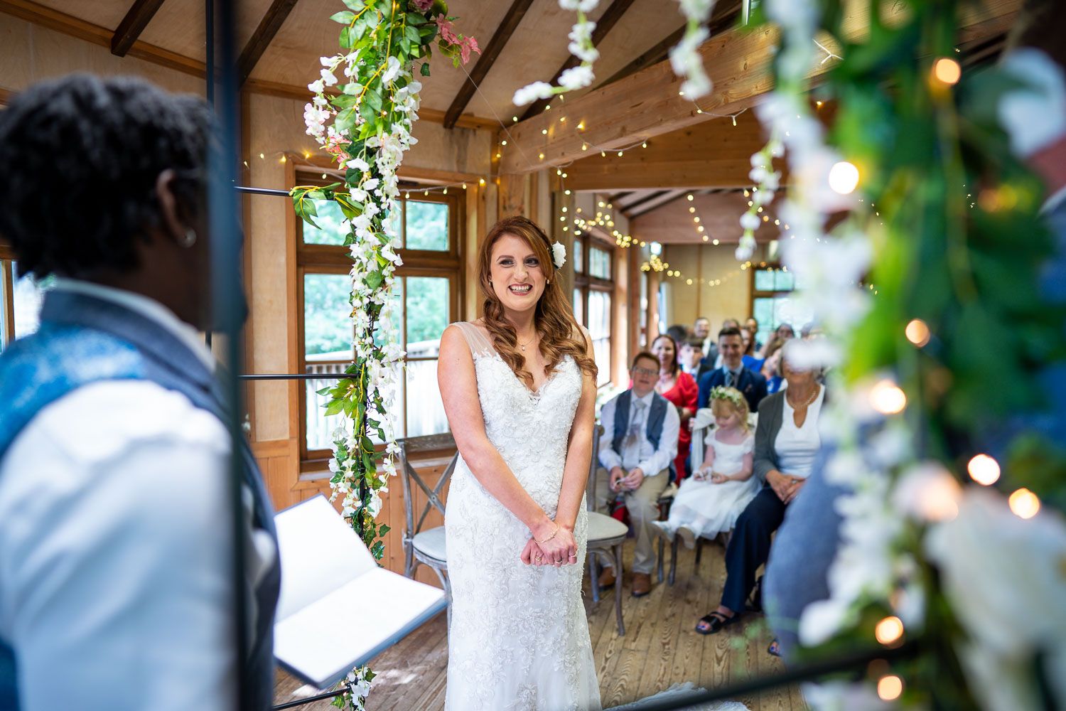 A joyful wedding ceremony takes place in a rustic indoor venue decorated with twinkling lights and greenery.