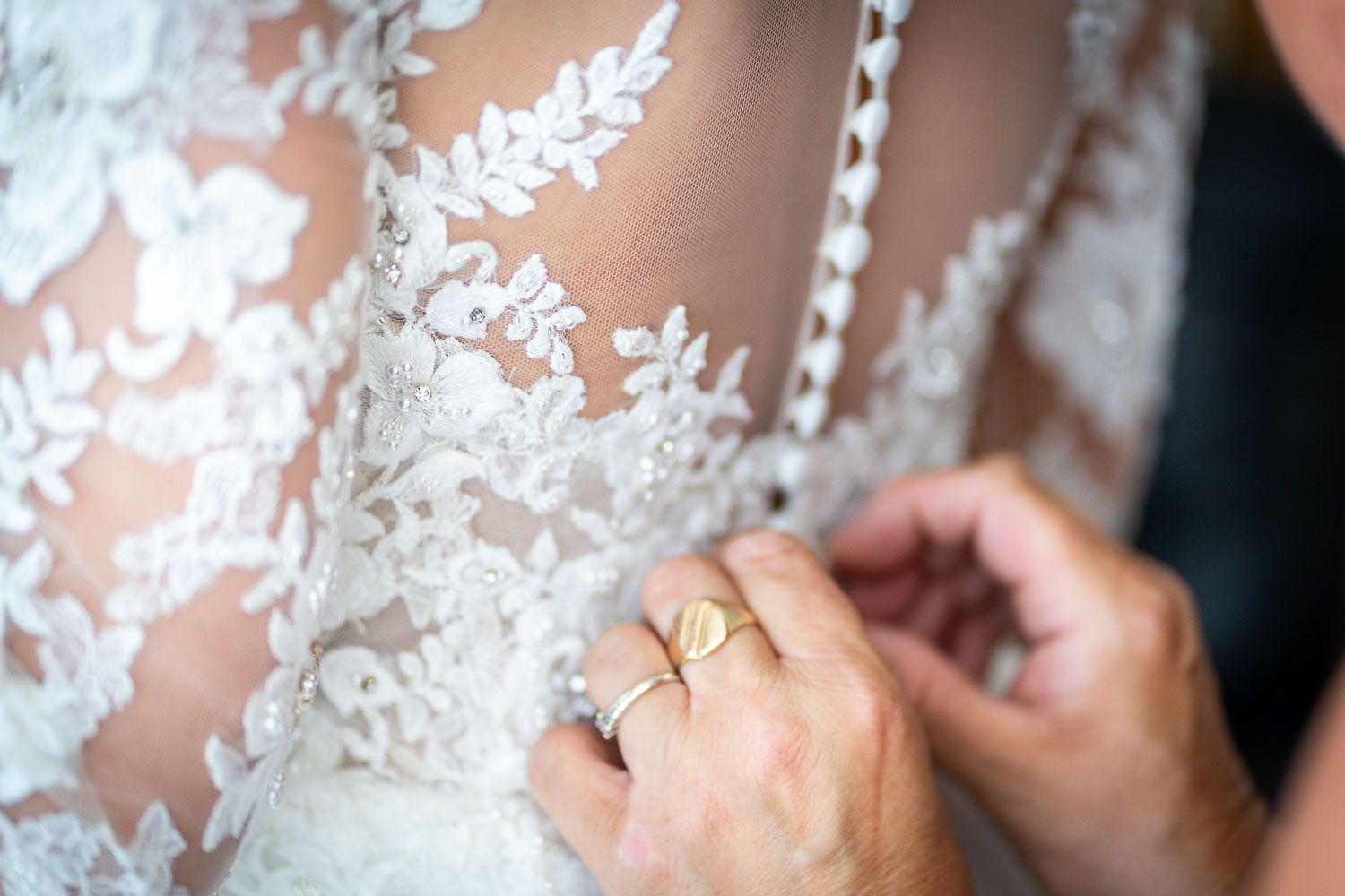 Close-up of delicate white lace details on a wedding dress with hands adjusting the fabric.