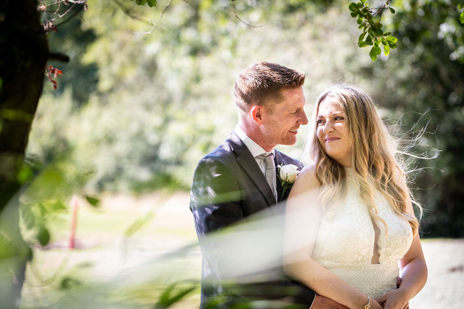 Two people share a romantic moment outdoors on a sunny day with natural bokeh and greenery in the background.