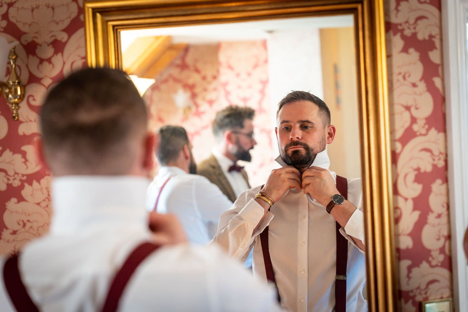 Someone adjusts their bow tie while getting ready in front of an ornate gold-framed mirror.
