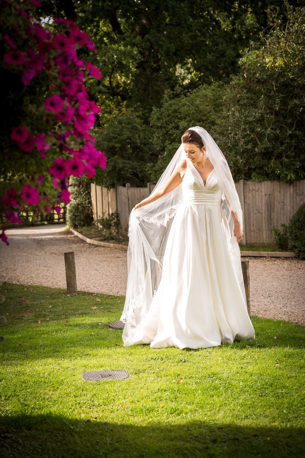 A flowing white wedding dress and veil in a garden setting with vibrant pink bougainvillea flowers and greenery.