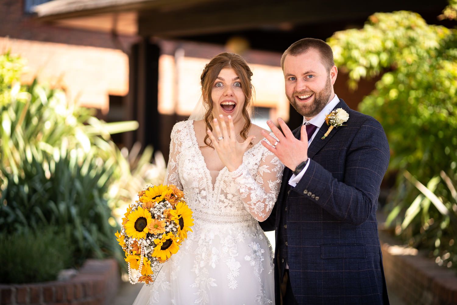 A joyful wedding couple sharing an excited moment outdoors with a bright sunflower bouquet in hand.