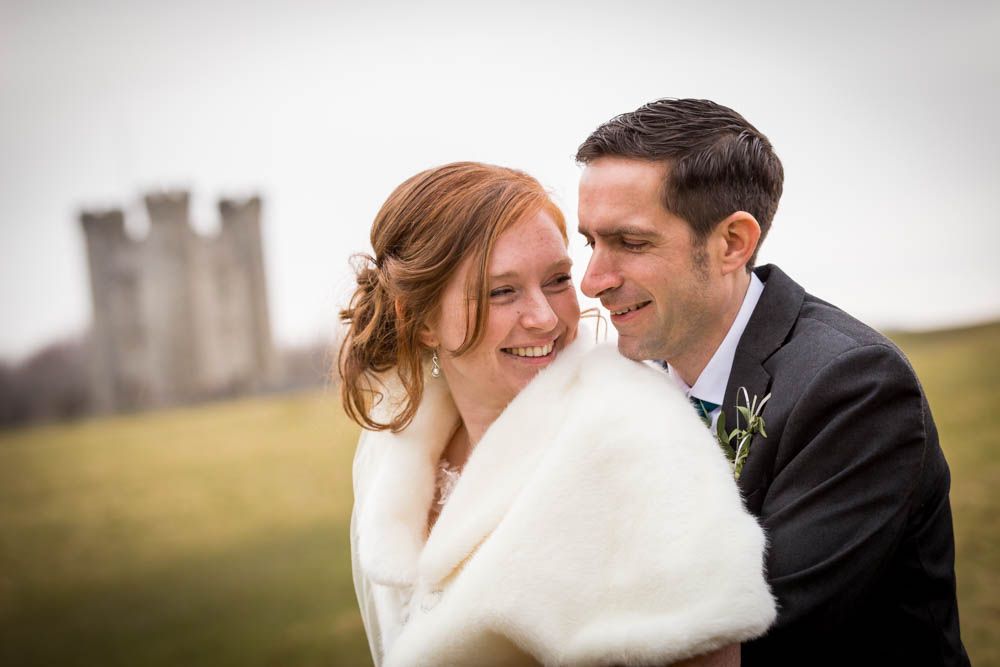 A romantic wedding moment shared between a couple embracing outdoors with a castle in the background.