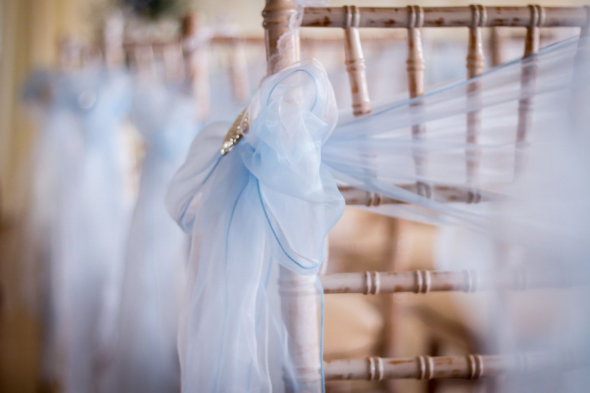 Light blue fabric bows decorate wooden chiavari chairs for an elegant wedding ceremony setup.