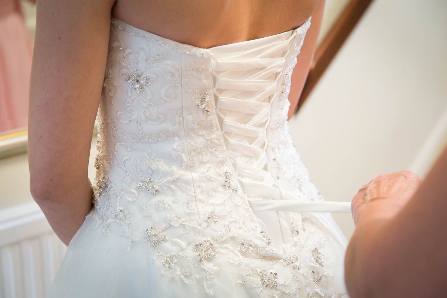Close-up detail of a white wedding dress showing intricate lace-up corset back with delicate embroidery and beading.