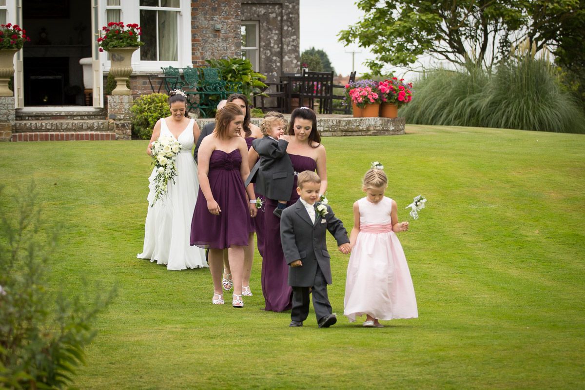 Wedding party members walking on a lush green lawn outside a stone building during a celebration.