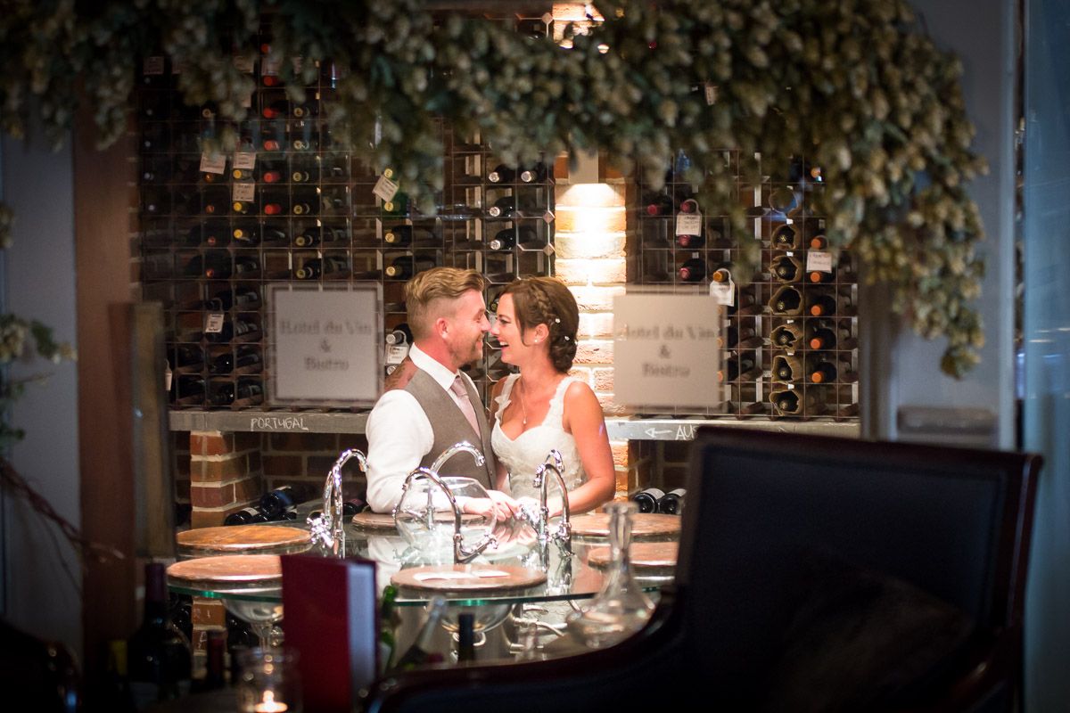 A couple shares an intimate moment at a wine bar with decorative ivy and bottle displays in the background.