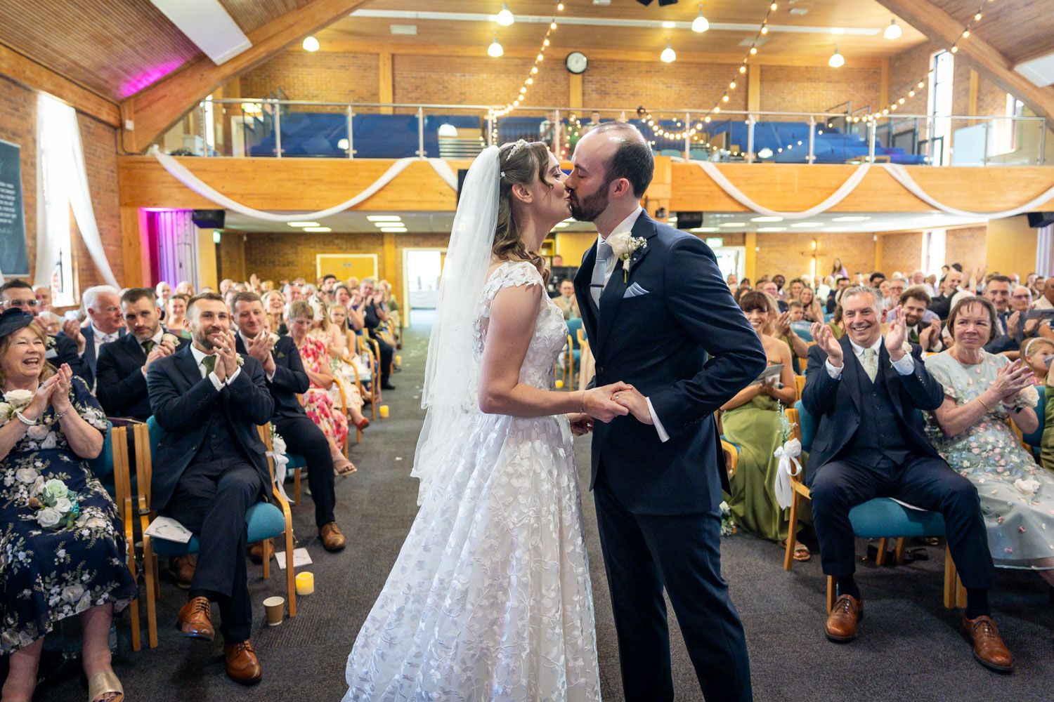 Bride and groom share their first kiss at the altar as wedding guests applaud in celebration.