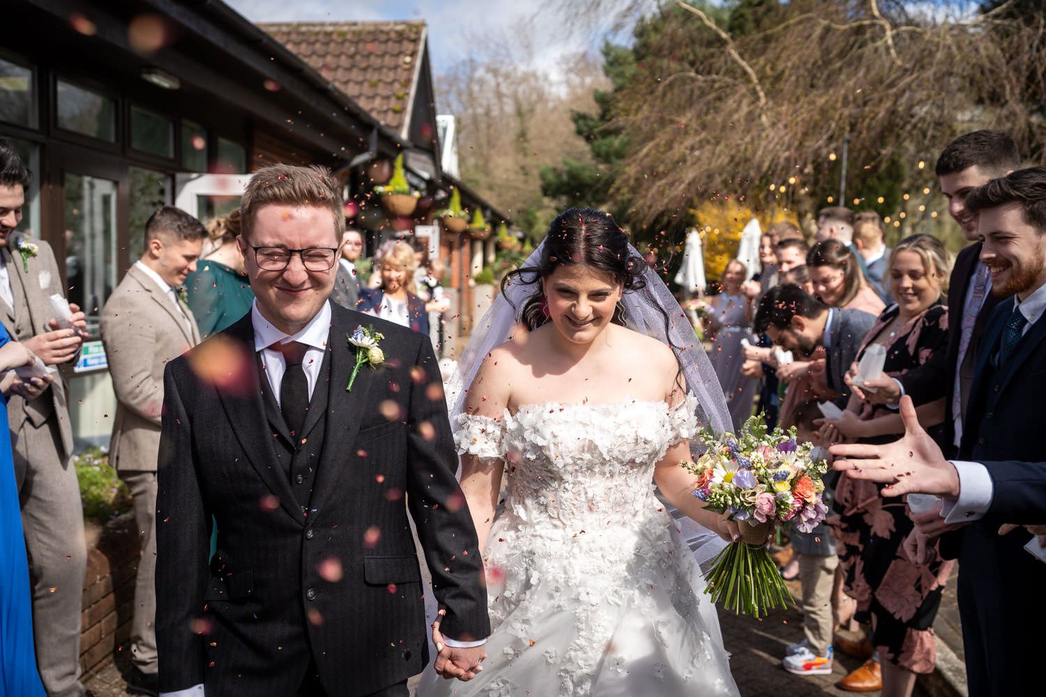 Wedding guests shower the happy couple with flower petals during a joyful outdoor celebration.