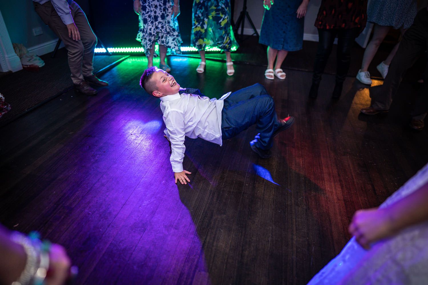 Someone showing off impressive dance moves on a dark dance floor illuminated by green and purple lights at a party.