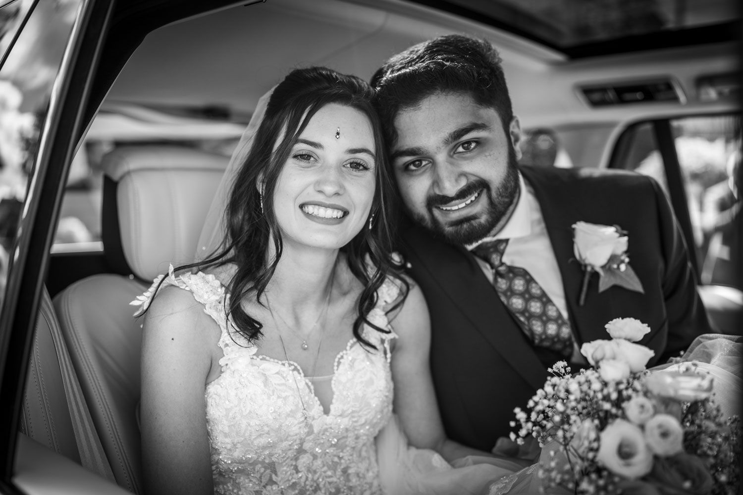A joyful wedding couple shares an intimate moment together in the back of a car.