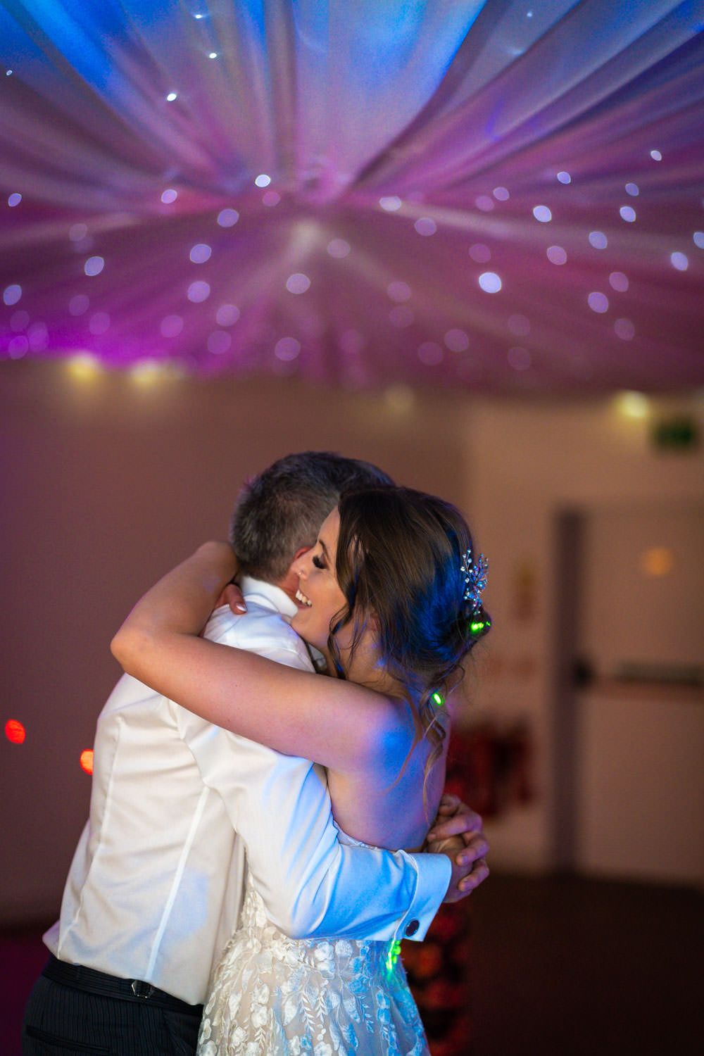 A couple embraces on the dance floor under colorful disco lights at a wedding reception.