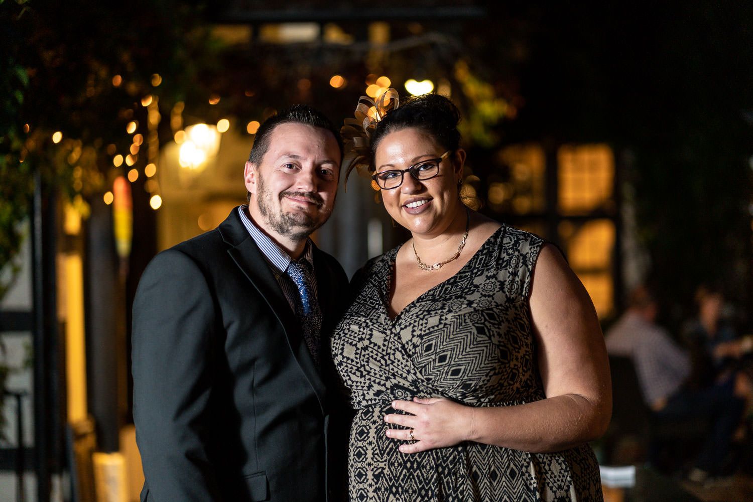 Elegant couple posing at an evening reception with warm glowing lights in the background.