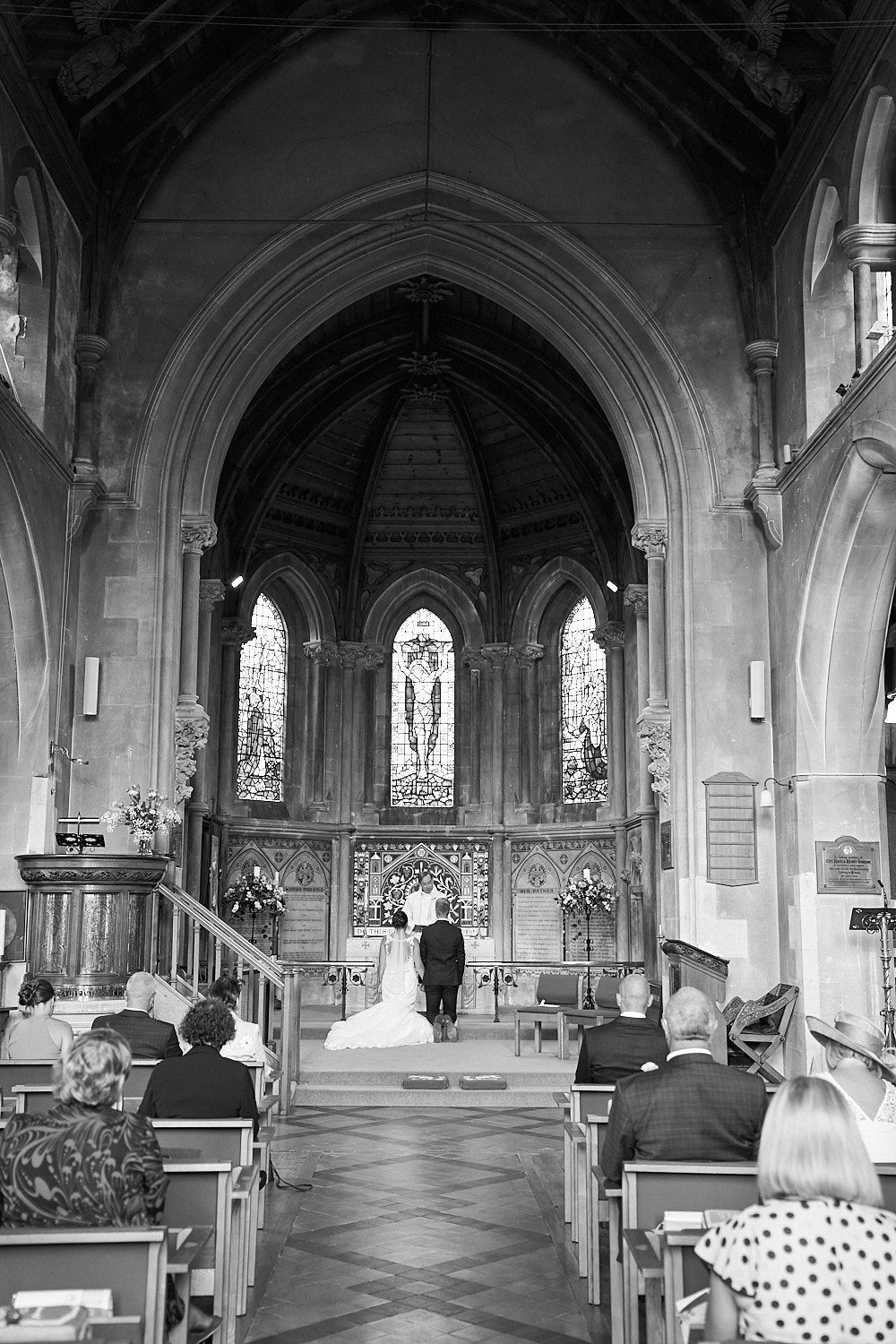 Black and white photo of a wedding ceremony inside a gothic church with stained glass windows and vaulted arches.