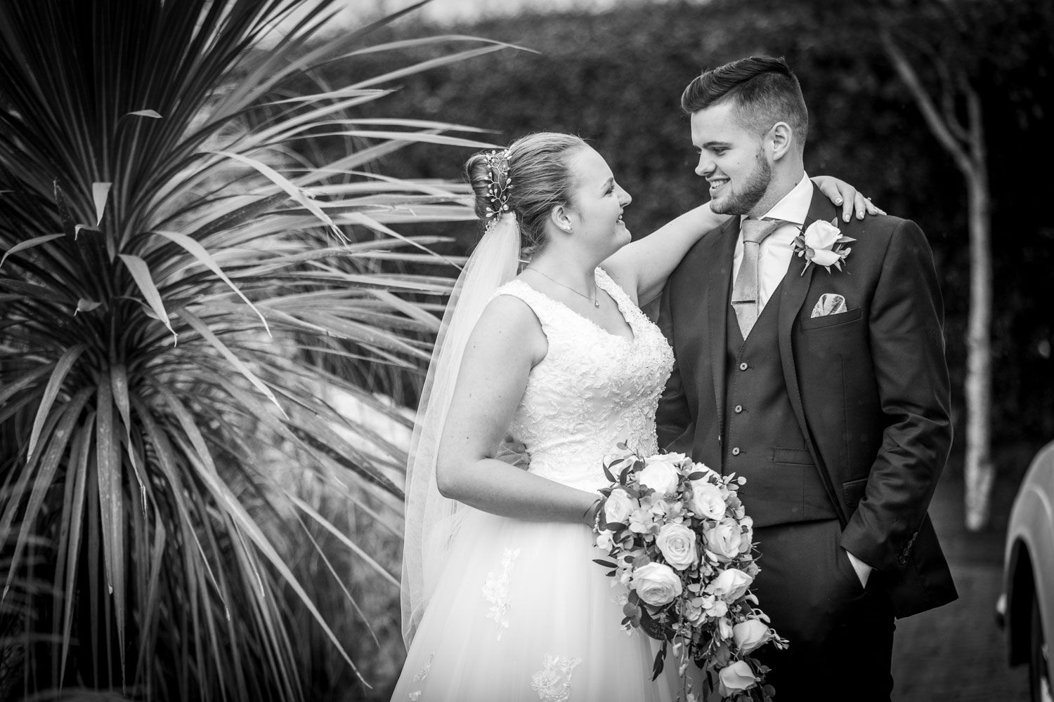 Black and white wedding portrait with tropical palm leaves in background.