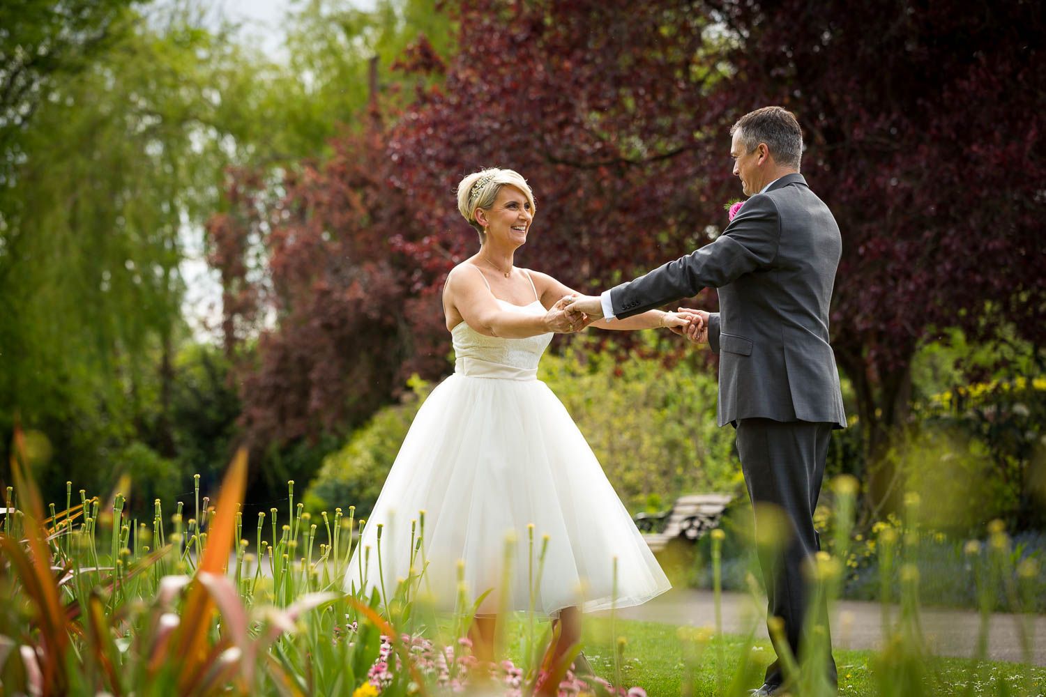 A romantic garden wedding photo with a couple dancing outdoors surrounded by vibrant flowers and foliage.