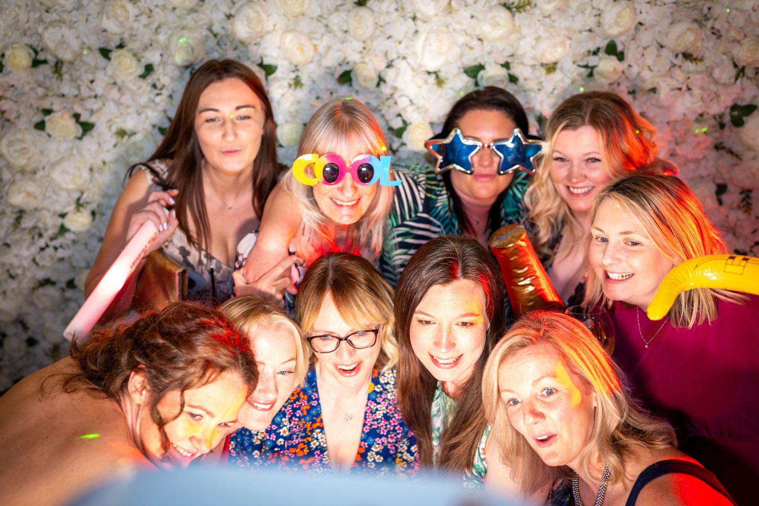 Group of people wearing colorful accessories huddled together for a fun photo against a speckled backdrop.