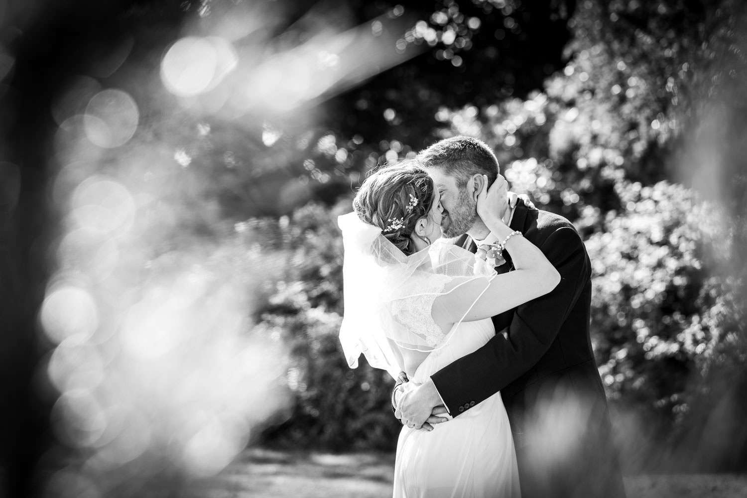 Black and white romantic kiss between bride and groom in dreamy garden.