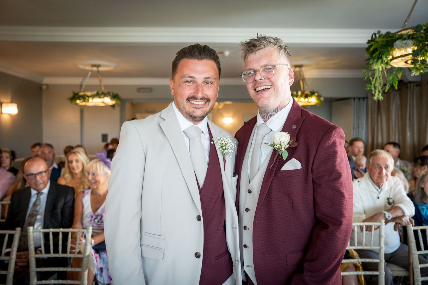 A pair in coordinated maroon and gray formal attire stand together at a wedding celebration.