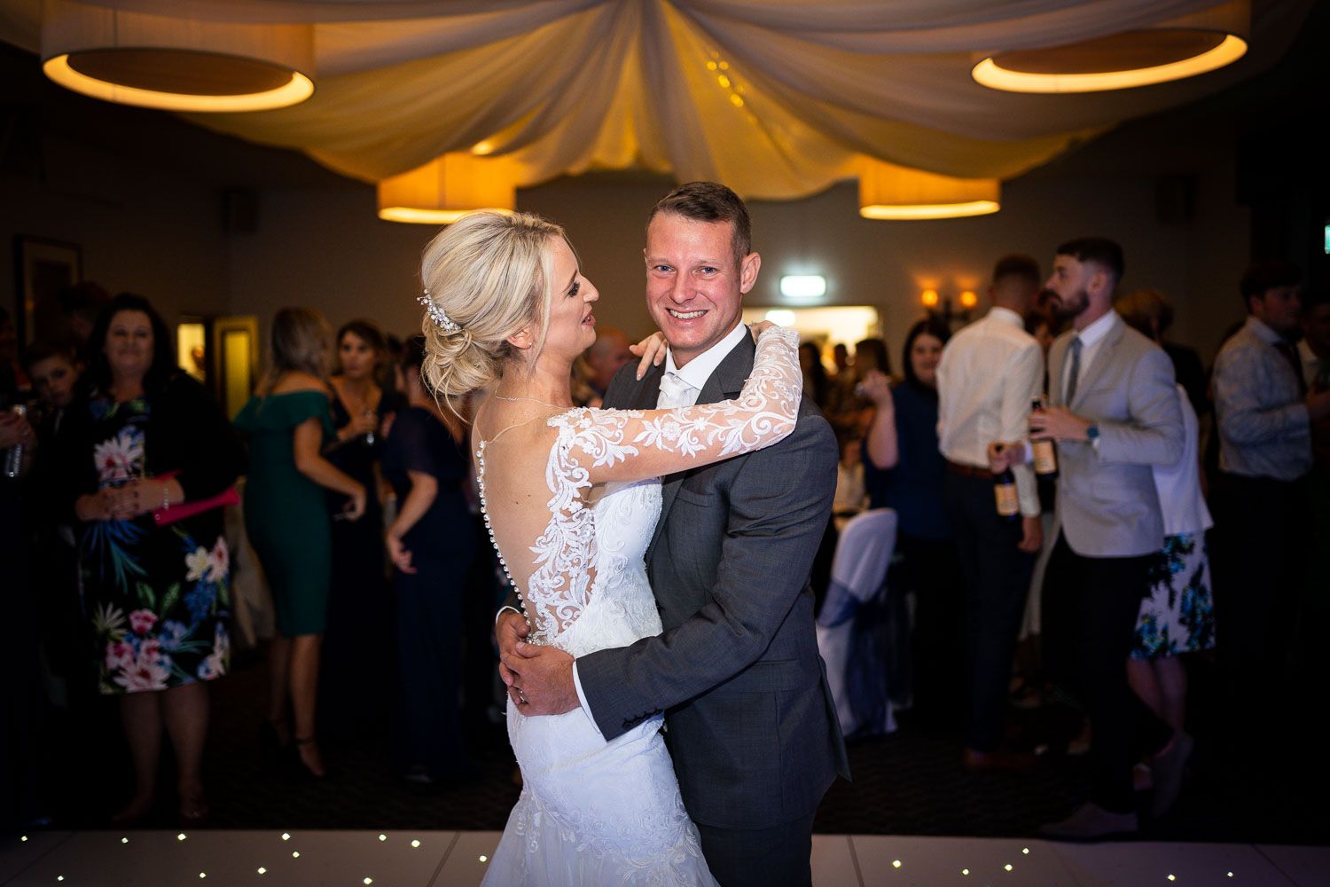 Couple share their first dance beneath elegant draped fabric ceiling at an indoor wedding reception.