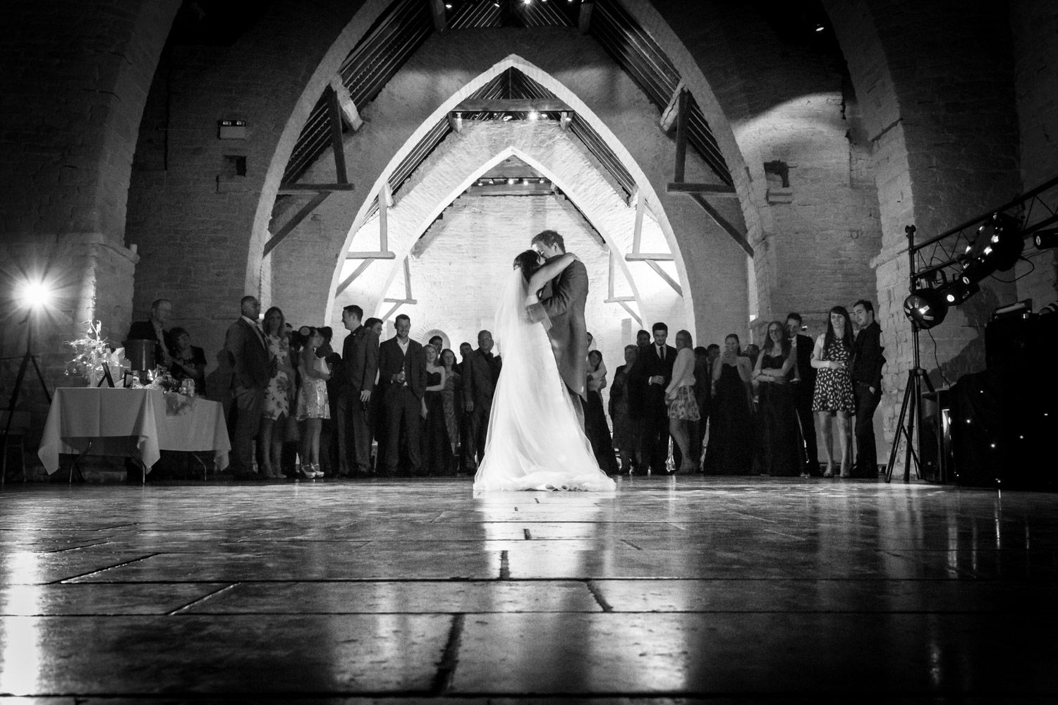 A couple shares their first dance at a wedding reception under dramatic gothic arches in black and white photography.
